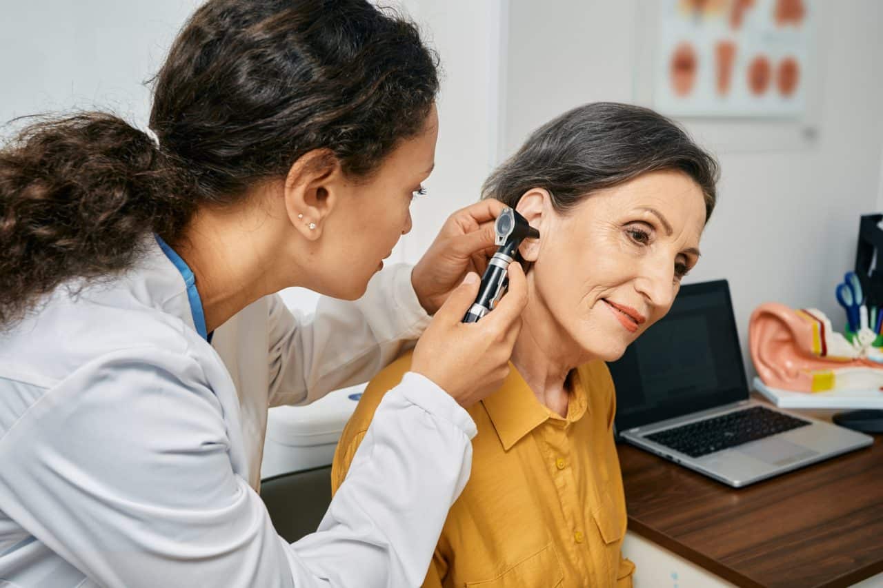 Audiologist examining the ear of a senior woman with hearing loss.