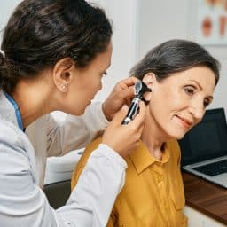 Audiologist examining the ear of a senior woman with hearing loss.
